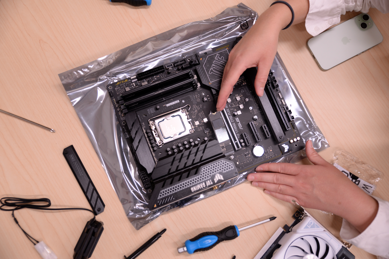 From above: hands touching a piece of electronic hardware, next to some tools on a desk surface